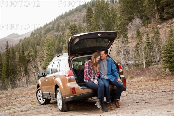 Portrait of young couple sitting in car trunk in non-urban scene