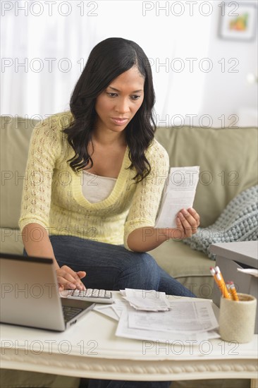 Woman using laptop and going through bills.