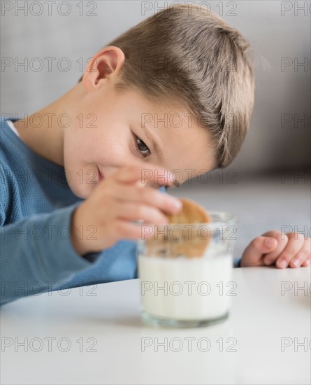 Boy (4-5) dipping cookie in milk.