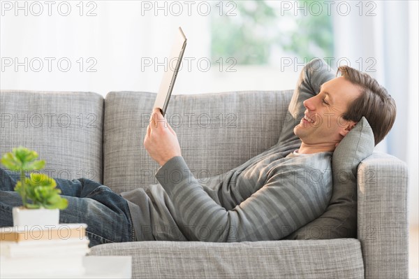 Man lying on sofa watching tablet pc.