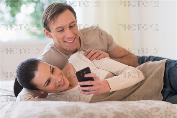 Couple lying on bed and looking at phone.