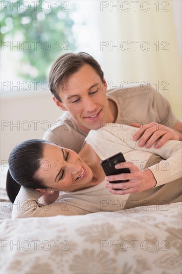 Couple lying on bed and looking at phone.