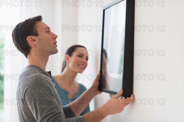 Couple hanging picture on wall.