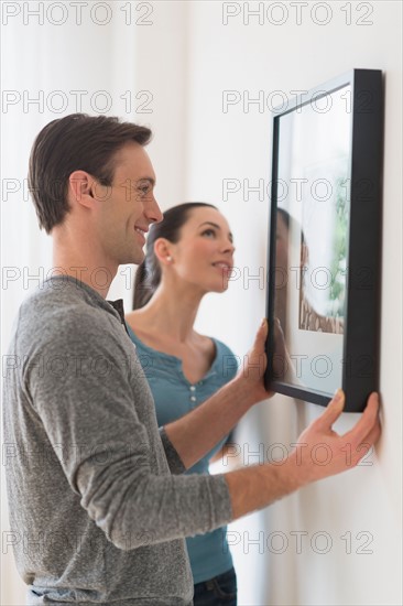 Couple hanging picture on wall.