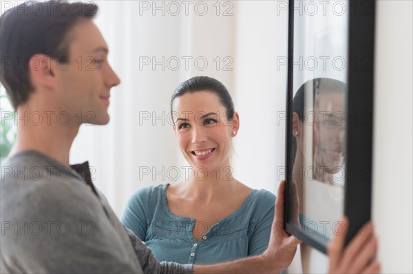 Couple hanging picture on wall.