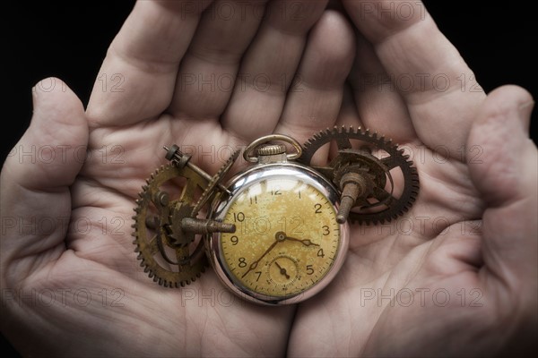 Hands holding antique clock and gears.