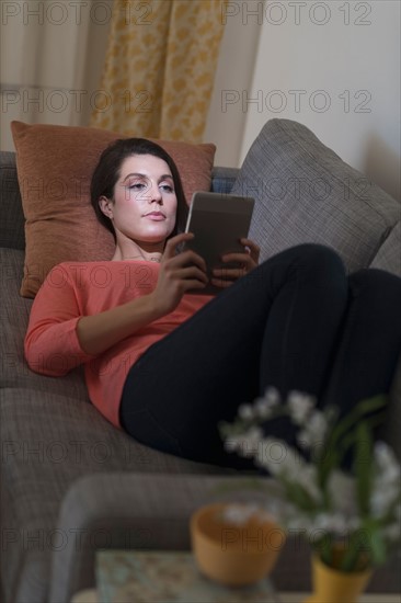 Woman using digital tablet while lying on sofa.