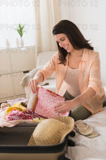 Woman packing suitcase in bedroom.