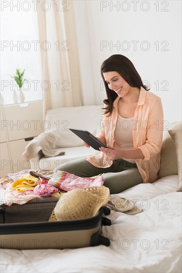 Woman using digital tablet while packing suitcase.