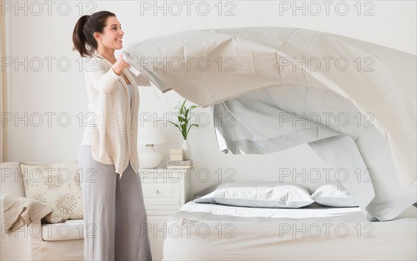 Woman spreading sheet on bed.