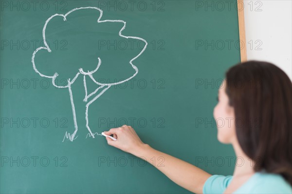 Woman drawing tree on blackboard.