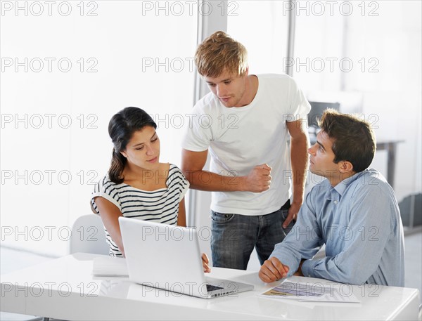 Coworkers talking at table, using laptop