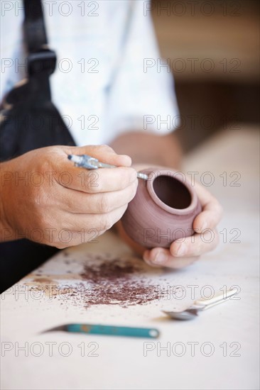 Close-up of male potter holding small vase, carving