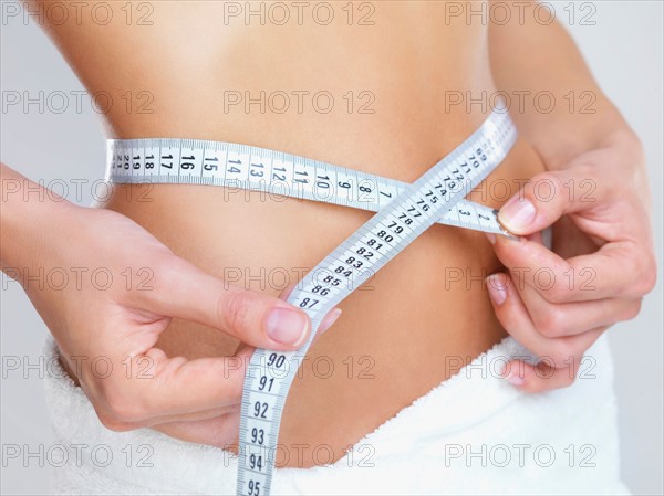 Studio Shot, Woman measuring her waist with tape measure