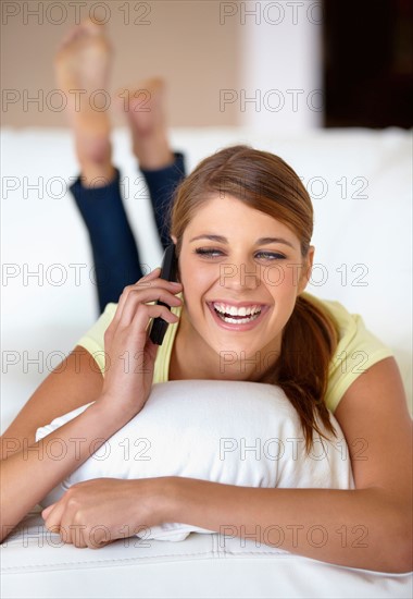 Young woman lying on bed and talking on phone