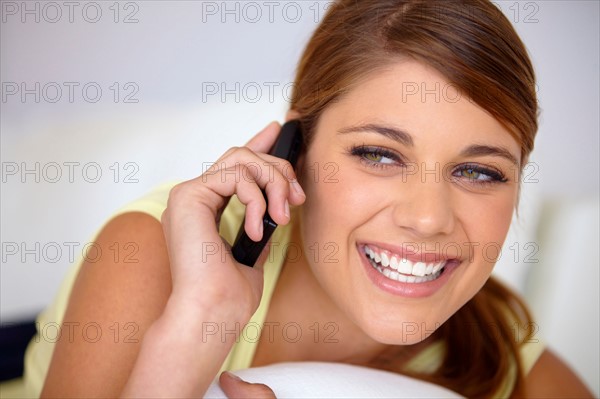 Young woman lying on bed and talking on phone