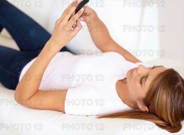 Young woman lying on bed and using cell phone