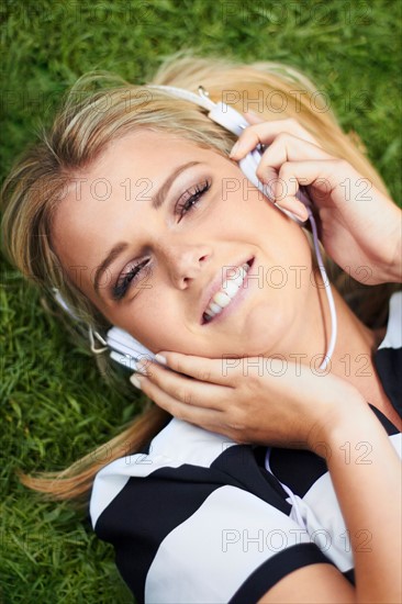 Portrait of young woman lying on grass and listening to music with headphones
