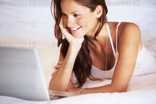 Woman using laptop while lying in bed