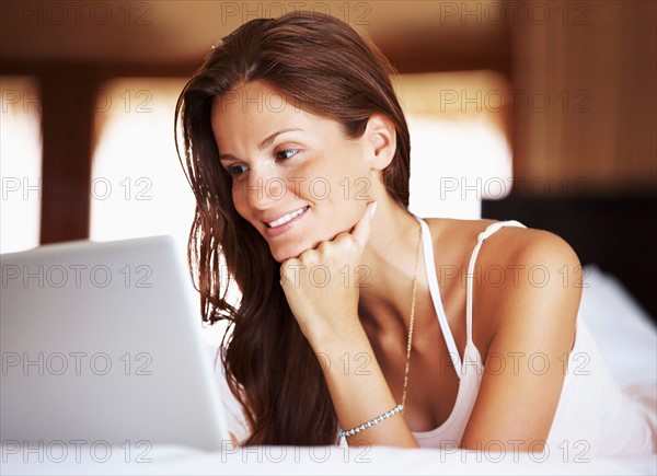 Woman using laptop while lying in bed