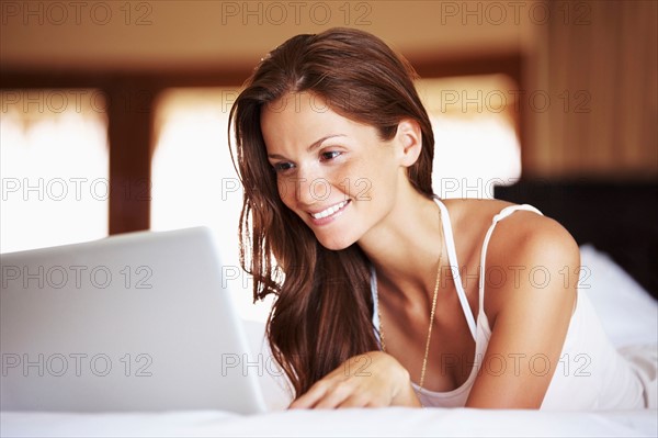 Woman using laptop while lying in bed