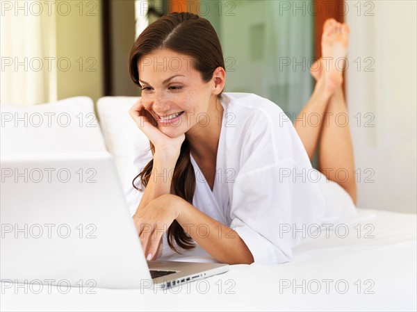 Woman using laptop while lying on bed