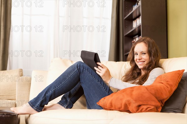 Smiling woman sitting on sofa with digital tablet