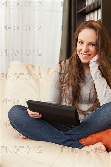 Smiling woman sitting on sofa with digital tablet