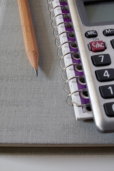 Calculator, textbook and pencil on notebook, studio shot