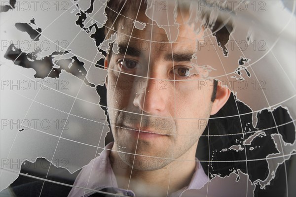 Studio portrait of man peering through translucent world map.