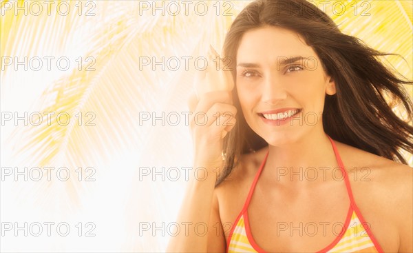 Woman holding shell, palm tree in background.
