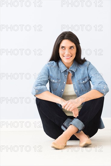 Studio portrait of young woman sitting on floor.