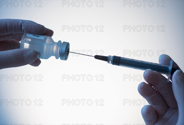 Close up of hands in surgical gloves preparing syringe for injection, studio shot.