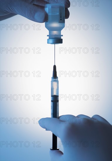 Close up of hands in surgical gloves preparing syringe for injection, studio shot.