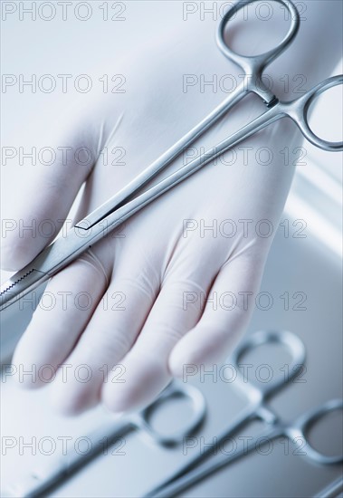 Close up of hand in surgical glove holding dental forceps, studio shot.