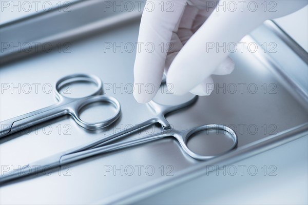 Close up of hand in surgical glove choosing dental forceps, studio shot.