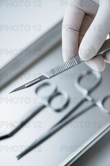 Close up of hand in surgical glove holding dental scalpel, studio shot.