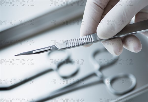 Close up of hand in surgical glove holding dental scalpel, studio shot.