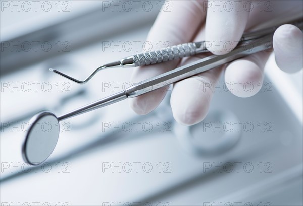 Close up of hand in surgical glove holding dental tools, studio shot.