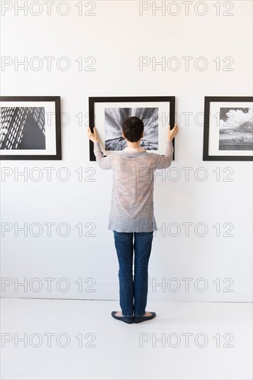 Woman hanging photographs in art gallery.