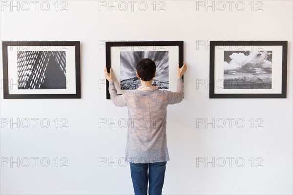 Woman hanging photographs in art gallery.