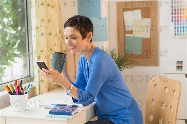 Woman using smart phone in home office.