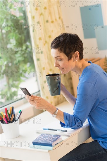 Woman using smart phone in home office.