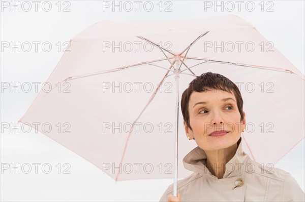 Portrait of smiling woman wearing raincoat and holding umbrella.