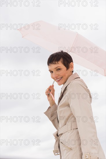 Portrait of smiling woman wearing raincoat and holding umbrella.