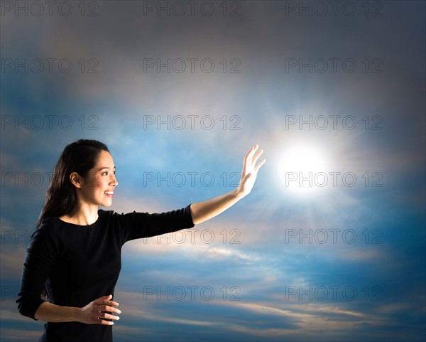 Woman reaching sun on sky, studio shot.
