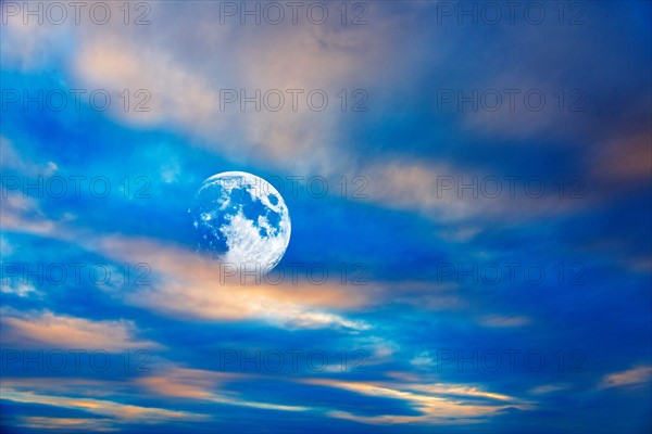 Moon behind clouds at dusk.