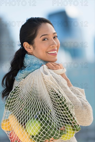 Portrait of smiling young woman with grocery shopping bag.