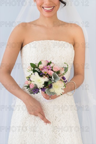 Bride in veil holding bouquet and crossing fingers.