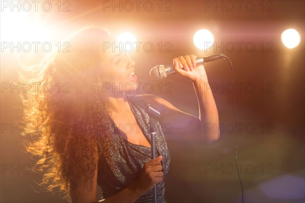 Young woman singing in spotlight.